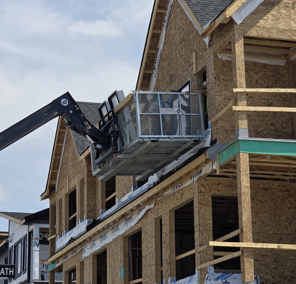 Galvanized ManBaskets work platform raised by a telehandler at a residential construction site